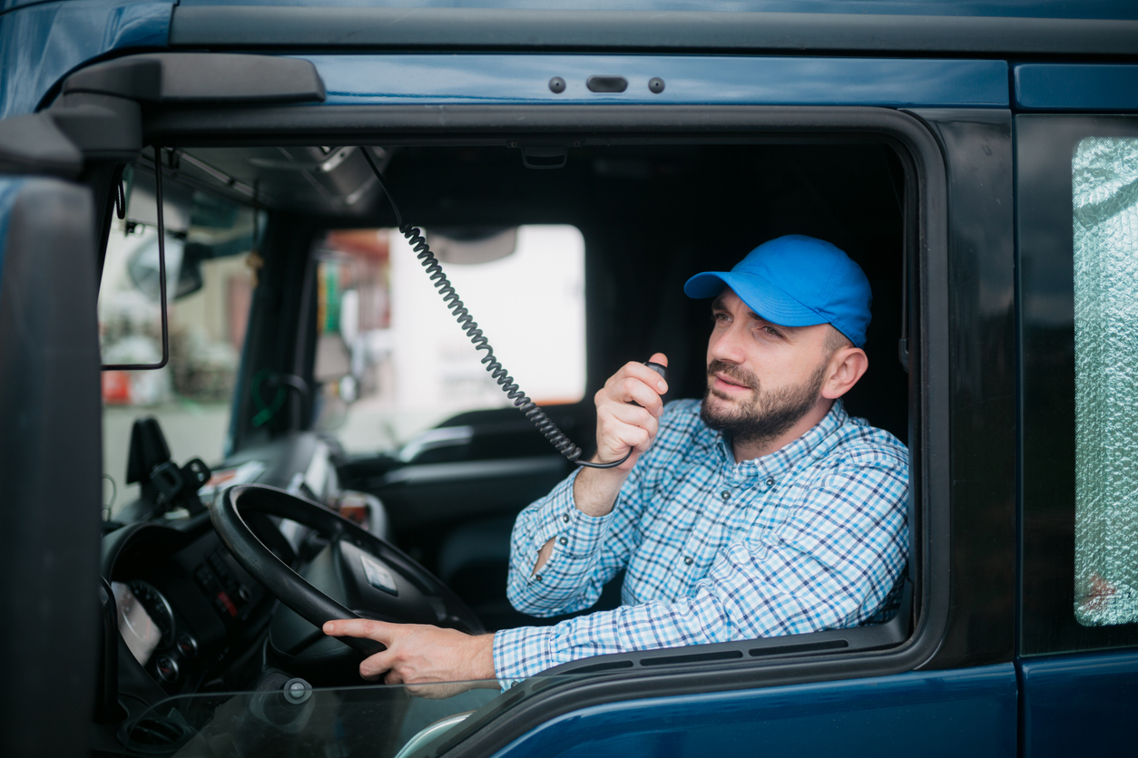 Middle aged truck driver sitting in a cabin of his truck and using a radio