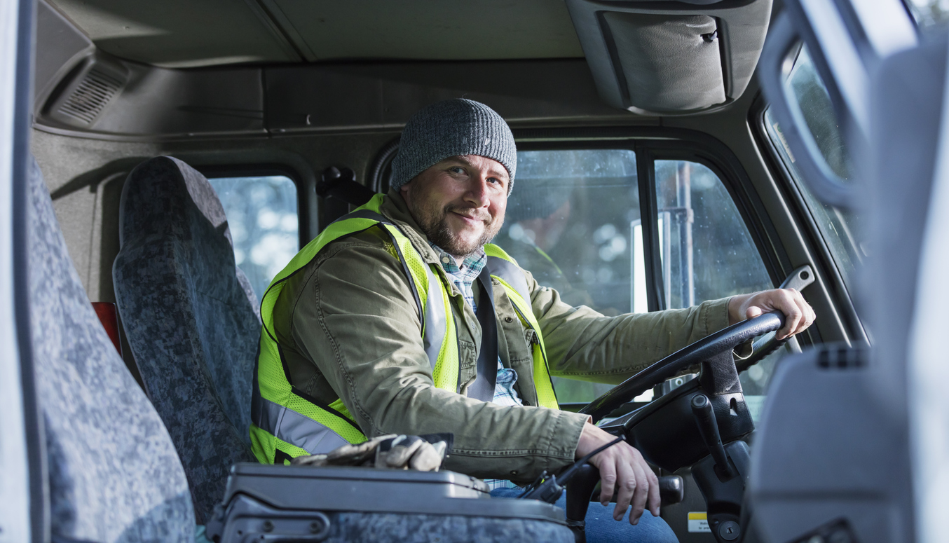 A mid adult Hispanic man in his 30s driving a truck. He is smiling at the camera.