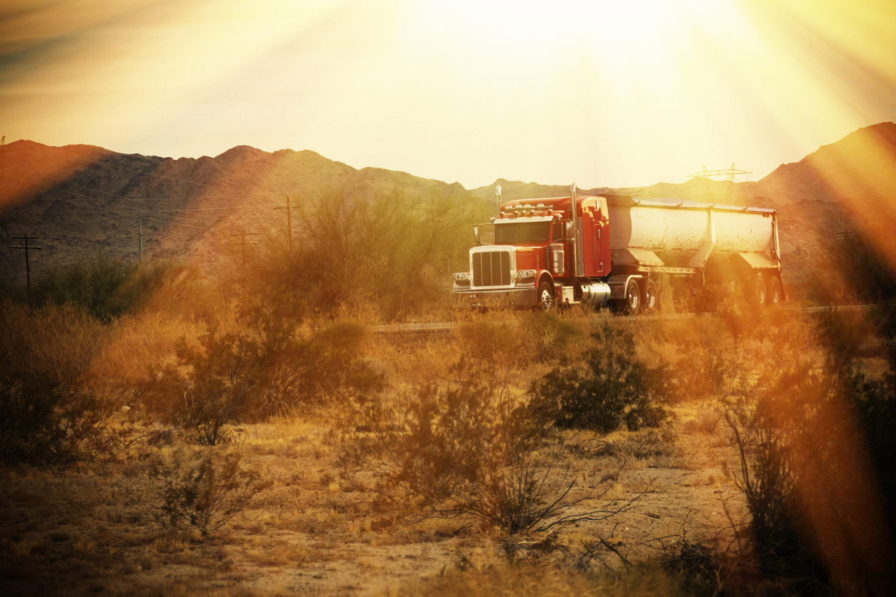 A semi truck heads down a desert road.