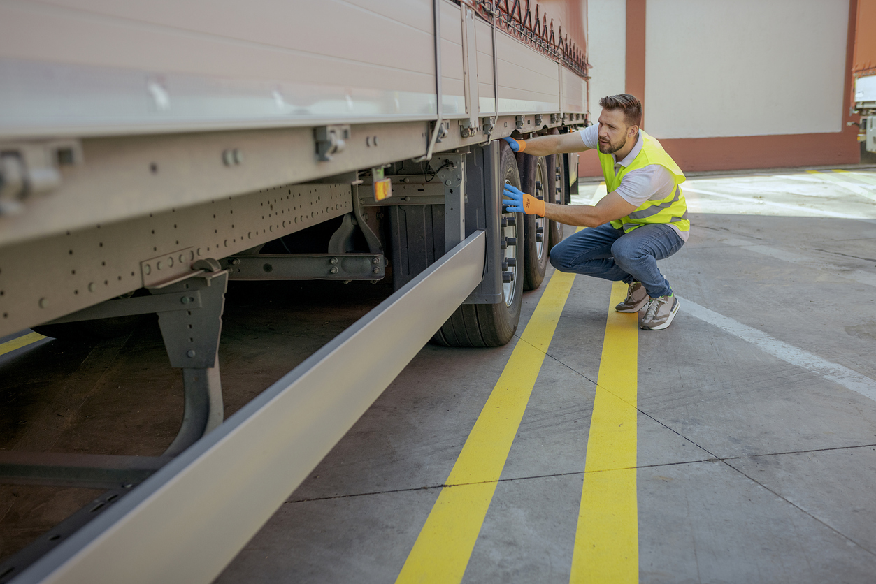 Truck Driver Inspecting Tires and Checking Depth of Tire Tread for Safe Ride