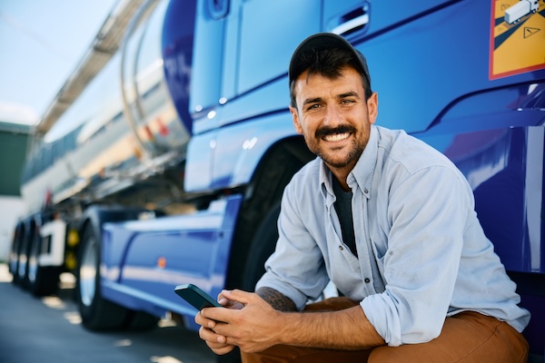 A happy truck driver using a cell phone in the parking lot of a truck stop health clinic