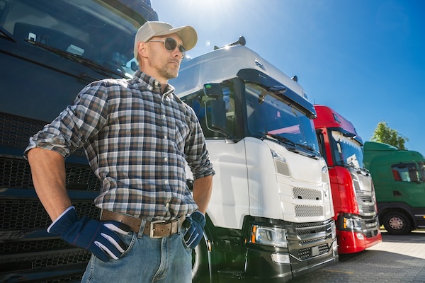 A semi truck driver standing in front of a group of trucks as a member of national trucking organizations