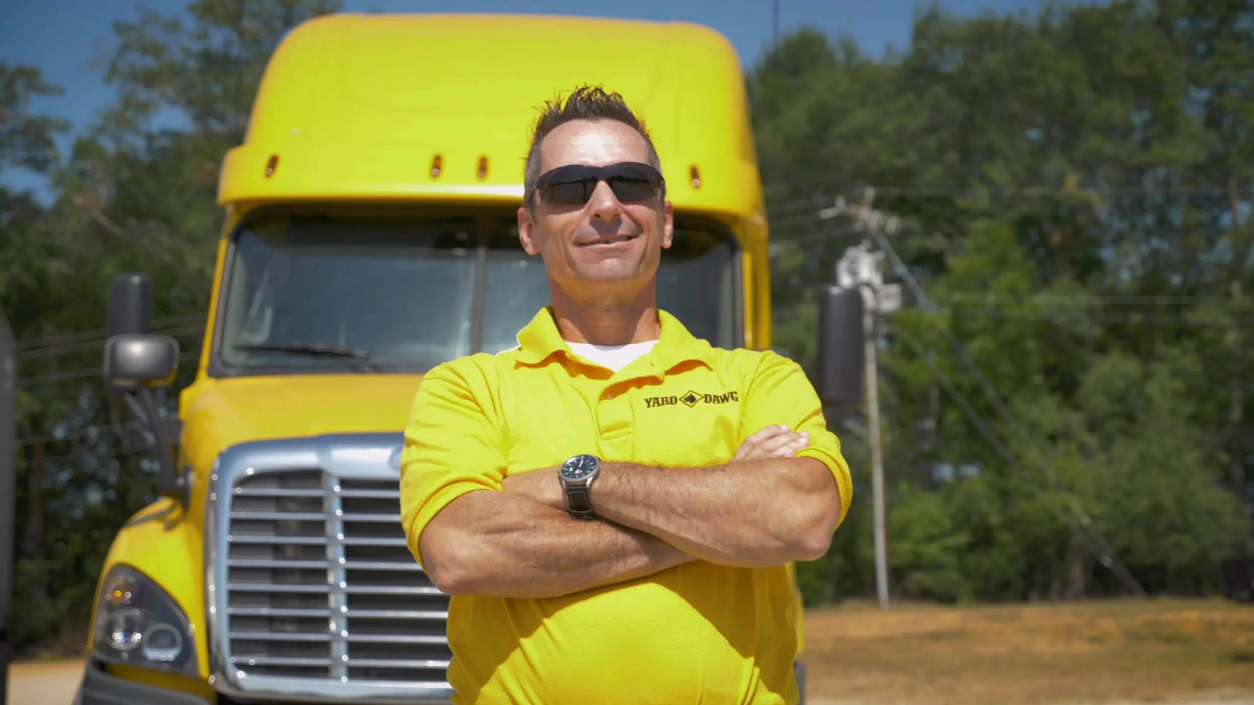 TDI Video 3 (first cut 9_26)_Moment 11 A man in a yellow shirt stands proudly in front of a yellow truck after passing his CDL classes.